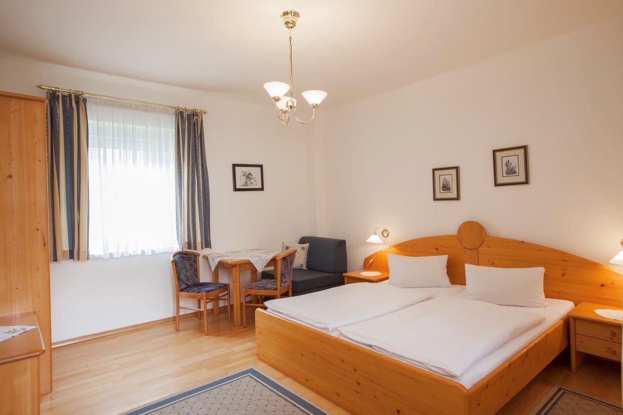 Ein gemütliches Hotelzimmer mit Doppelbett, Holzmöbeln und einem kleinen Tisch mit Stühlen.