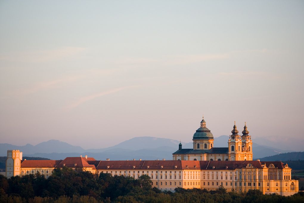 Stift Melk in Österreich bei Sonnenuntergang mit Bergen im Hintergrund.