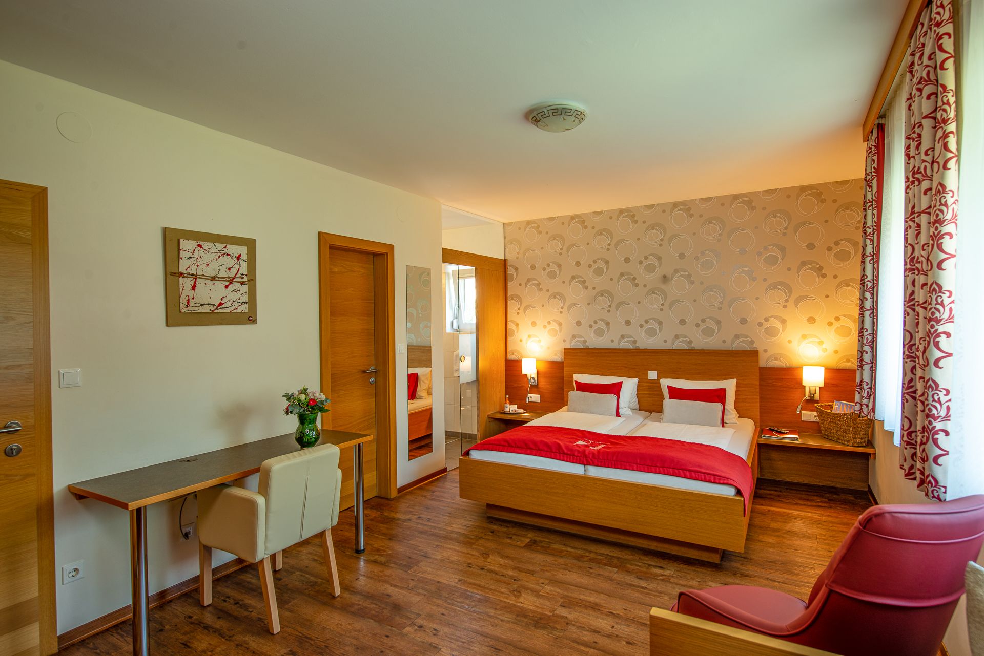 Hotelzimmer mit Doppelbett, Schreibtisch, Stuhl und rotem Sessel.