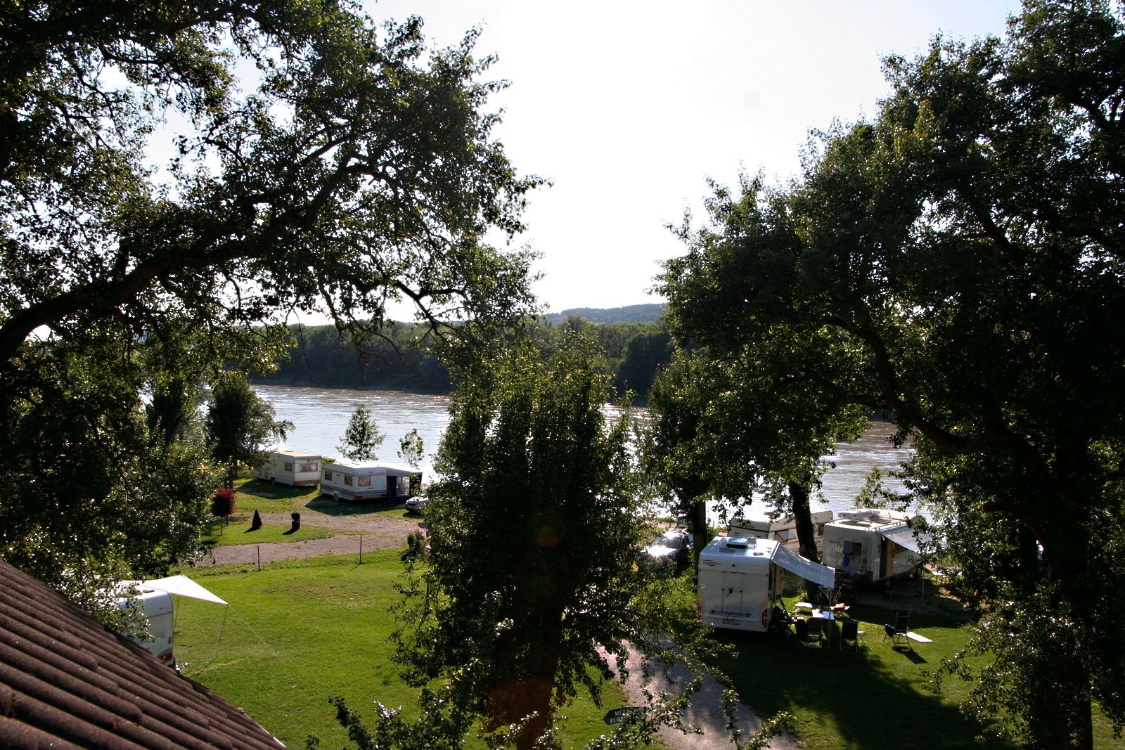 Campingplatz am Fluss mit Wohnwagen und Bäumen.