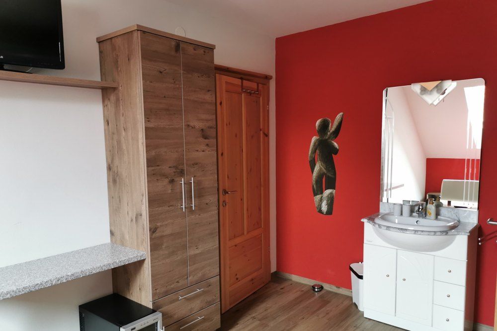 Zimmer mit roter Wand, Holzschrank, Waschbecken und Spiegel.