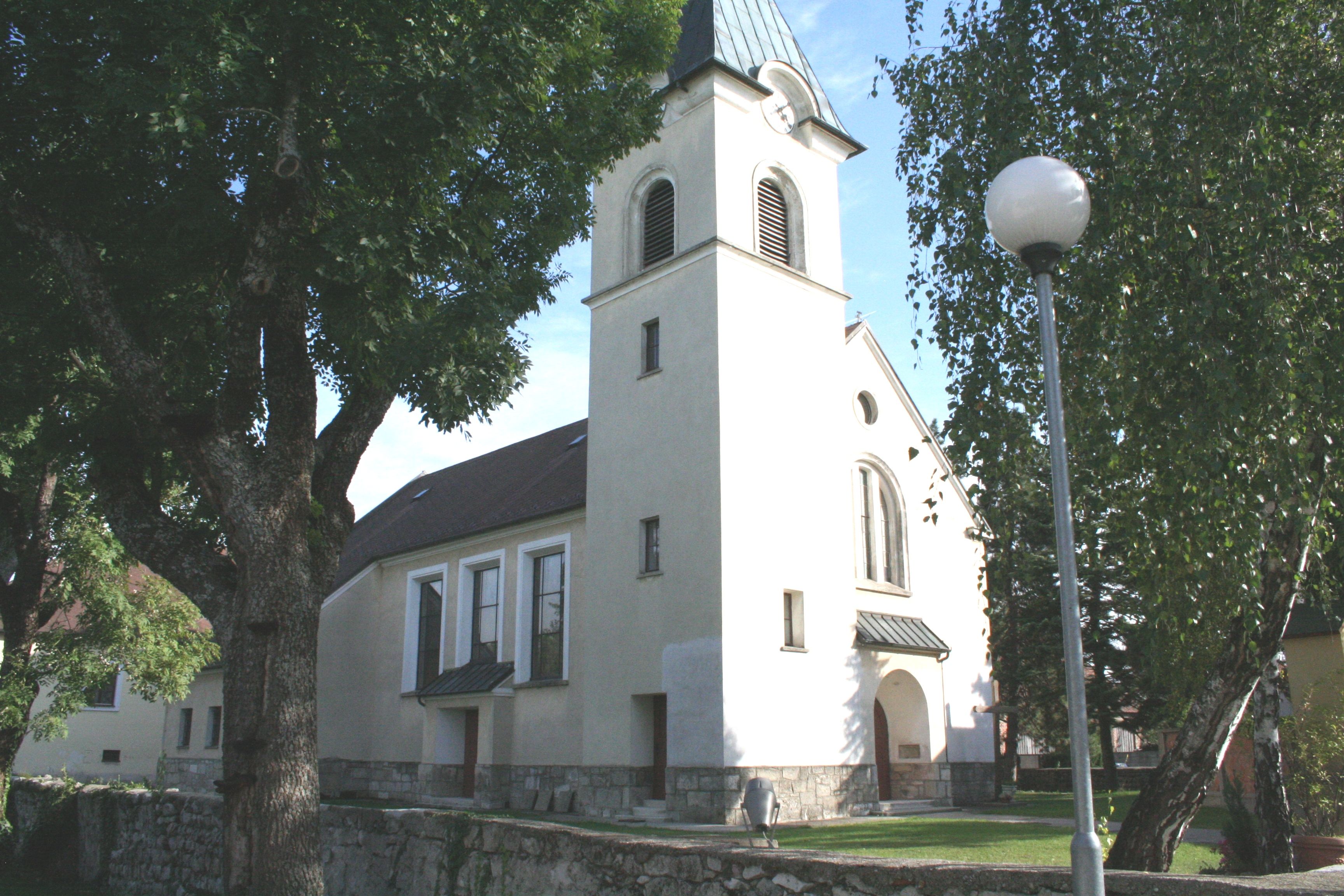 Kirche in Pischelsdorf mit Turm und Bäumen im Vordergrund.