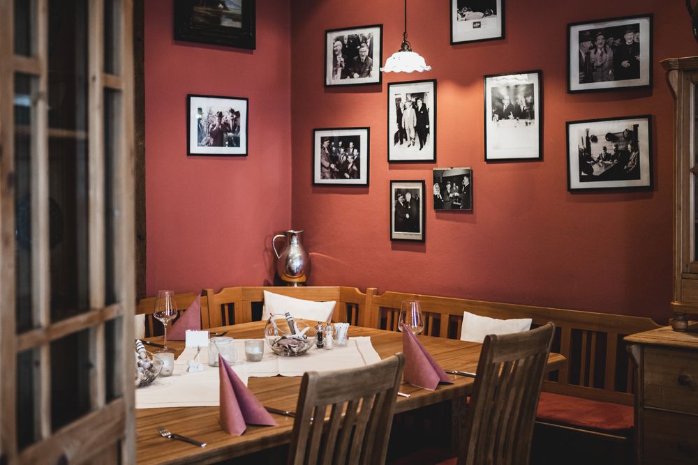 Gemütliches Restaurant mit Holztisch, roten Wänden und gerahmten Fotos.