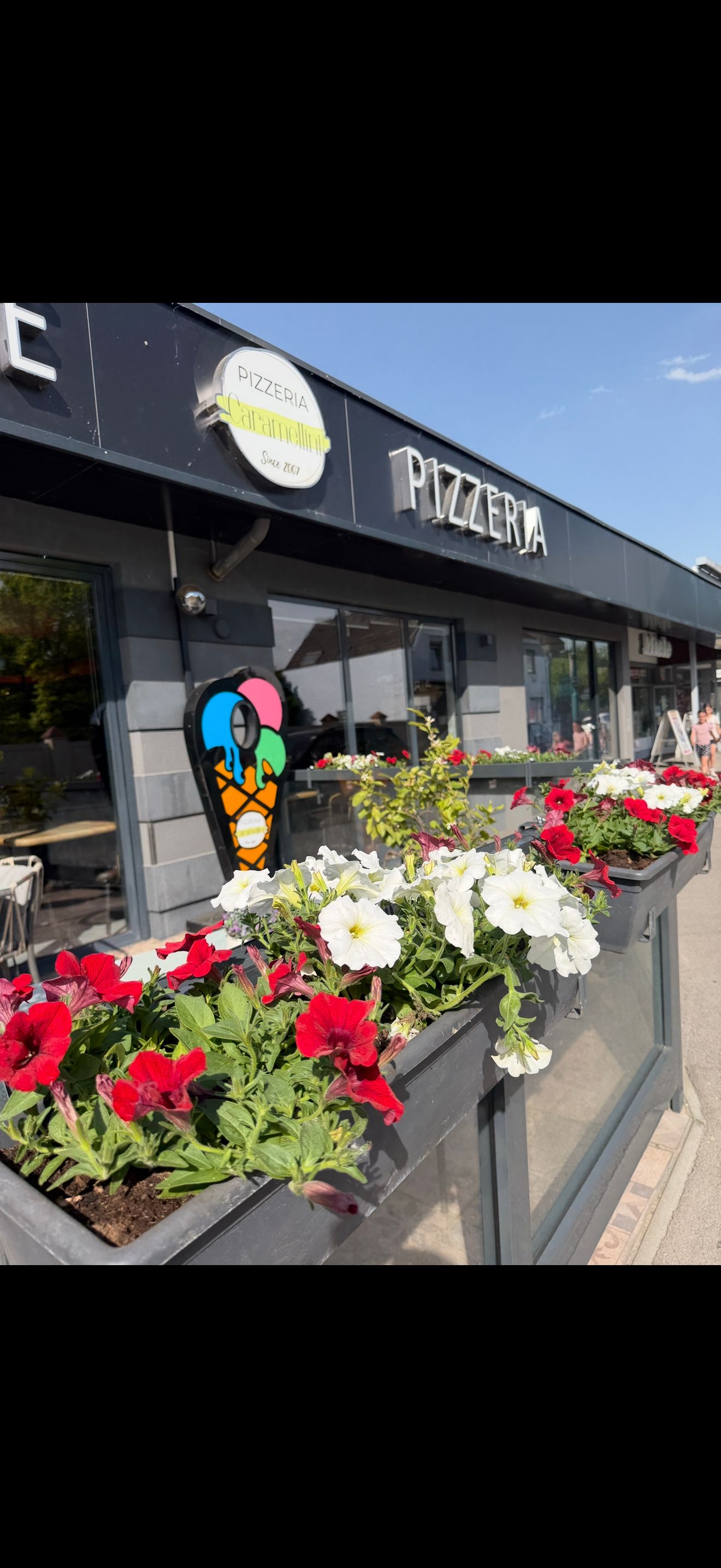 A Pizzeria Caramellini külső nézete virágokkal és fagylaltozóval.