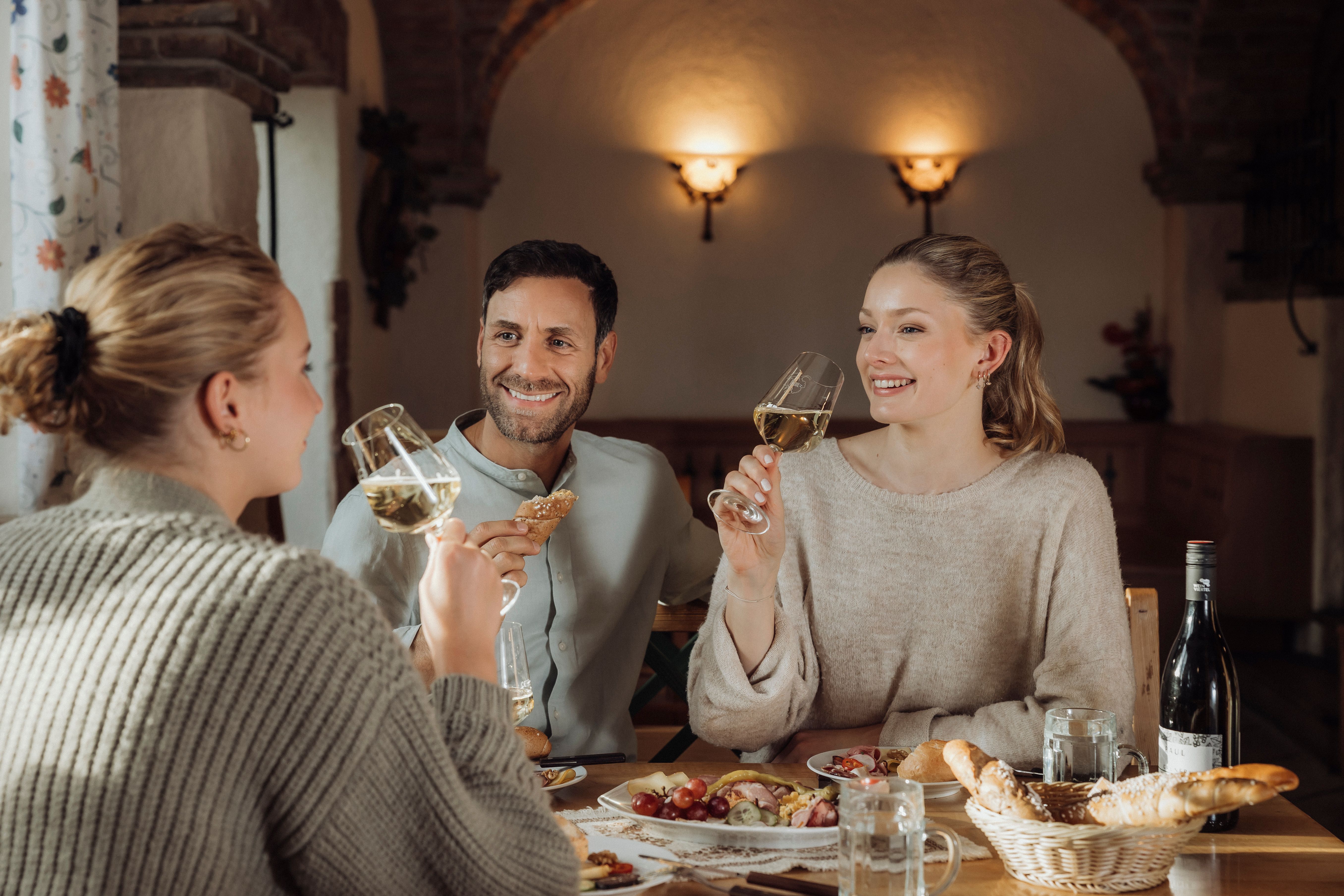 In einer gemütlichen Runde genießen die Freunde ein köstliches Brettljause und erfrischenden Wein, während sie anstoßen und lachen. Die Atmosphäre ist geprägt von der herzlichen Gastfreundschaft der Heurigenkultur, die hier im Weinviertel lebendig wird.