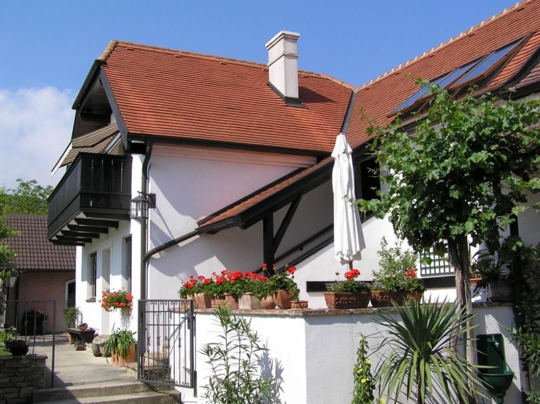 Ein weißes Haus mit rotem Ziegeldach, Balkon und Garten mit Pflanzen und Blumen.