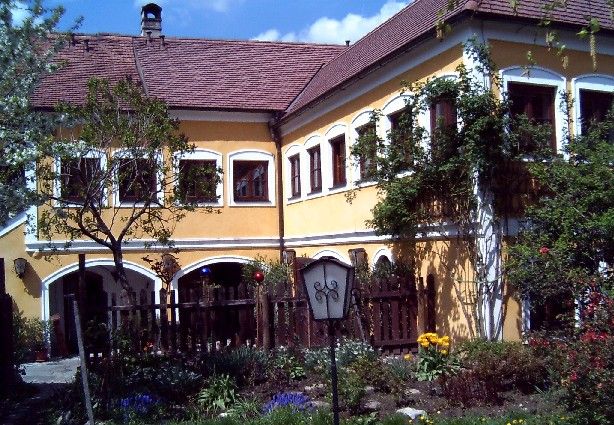 Žlutý dům s červenými střešními taškami a zahradou v popředí.
