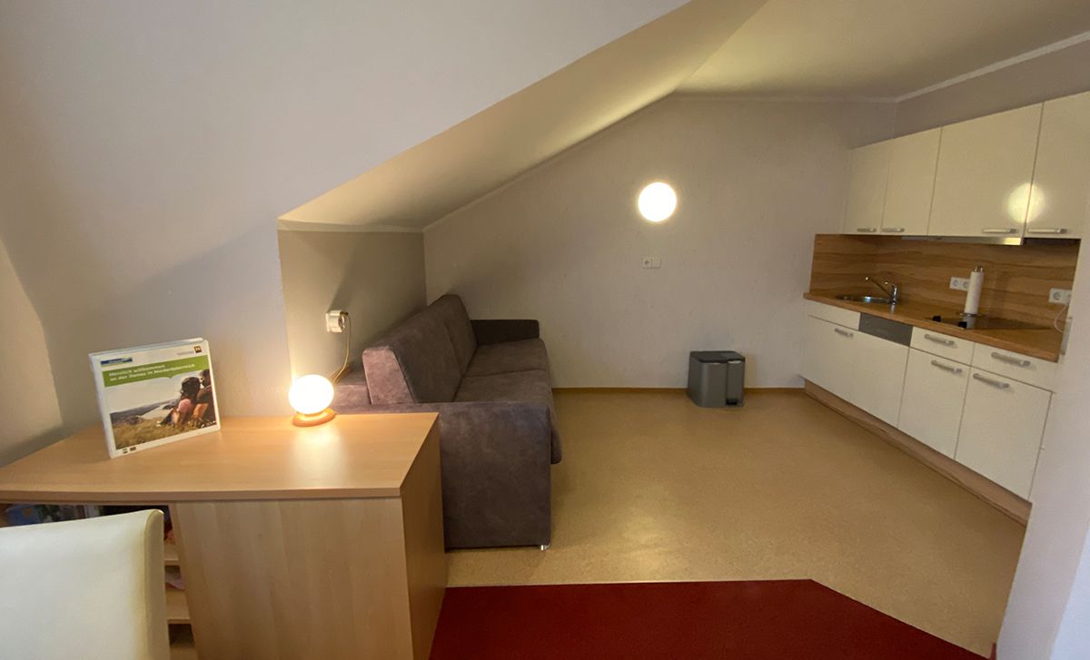 Innenansicht einer Ferienwohnung mit Sofa, Tischlampe und Küchenzeile.