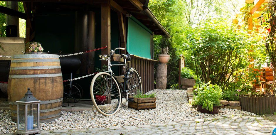 Rustikaler Eingangsbereich mit Fahrrad, Holzfass und Pflanzen.