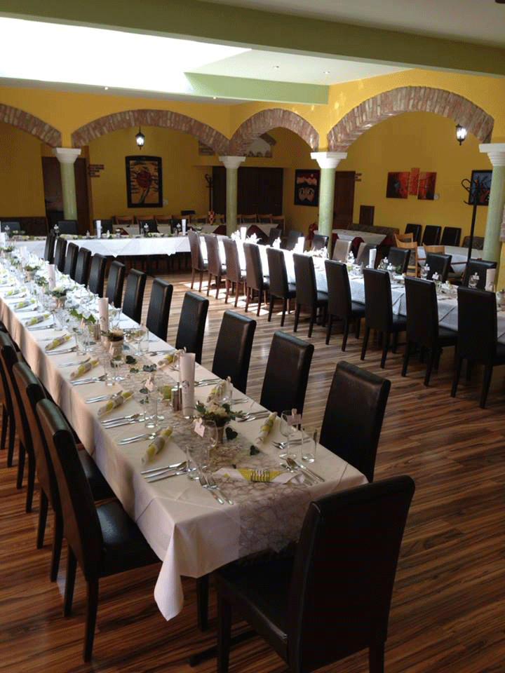 Festlich gedeckte Hochzeitstafel in einem Raum mit gelben Wänden und Backsteinbögen.