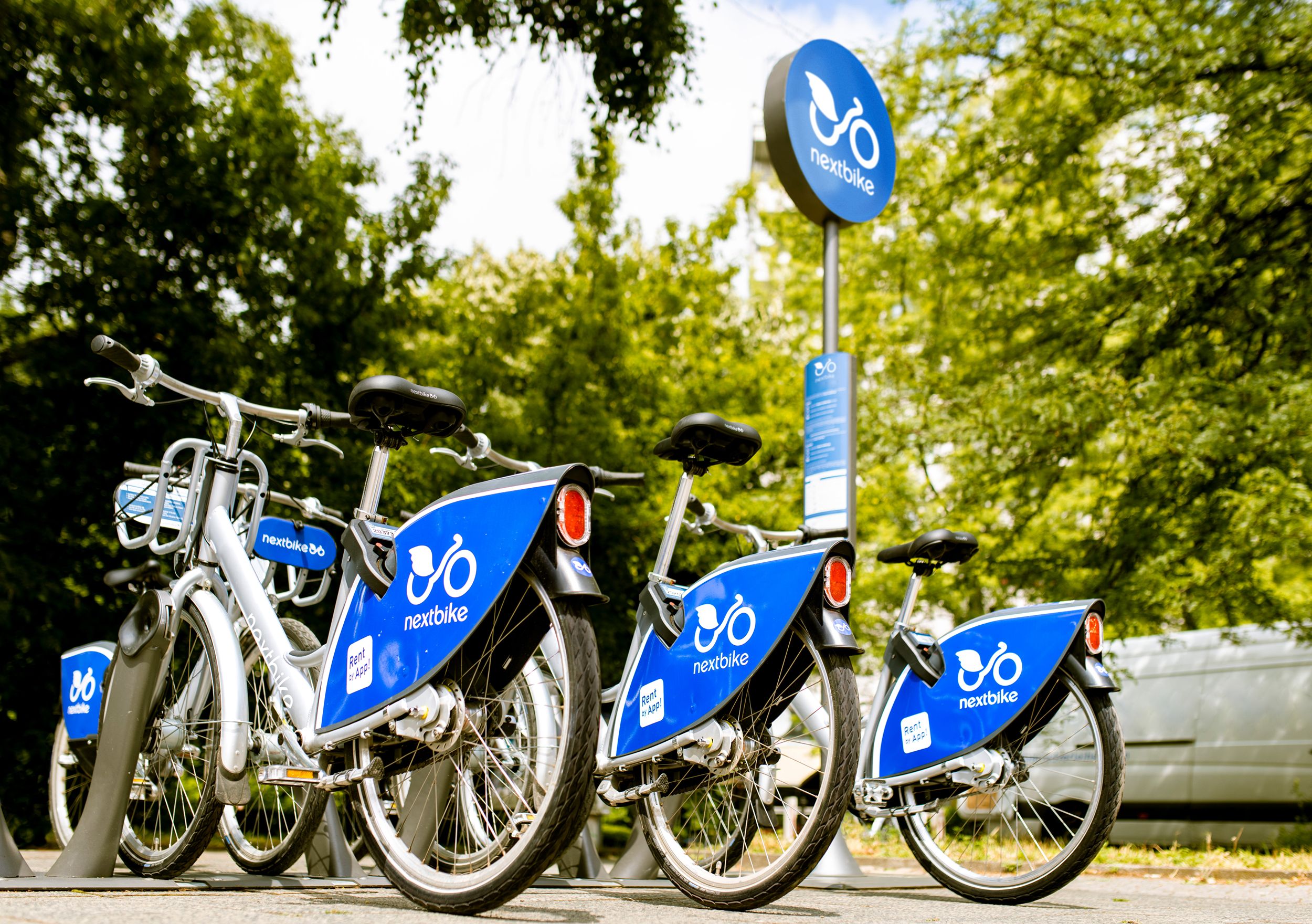 Több Nextbike kerékpár egy fákkal körülvett szabadtéri állomáson.