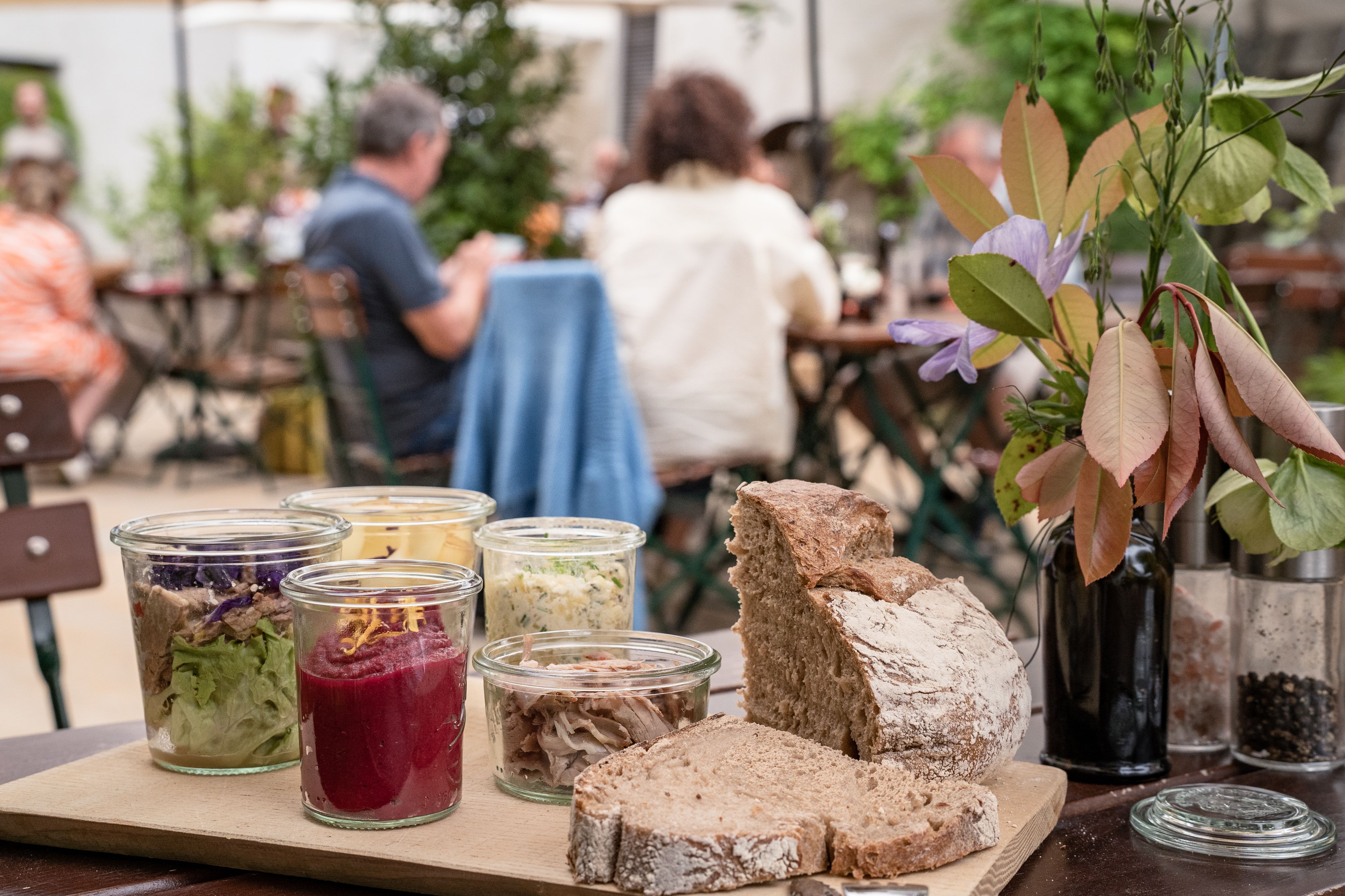 Leute sitzen im Innenhof, im Vordergrund Essen in kleinen Gläsern