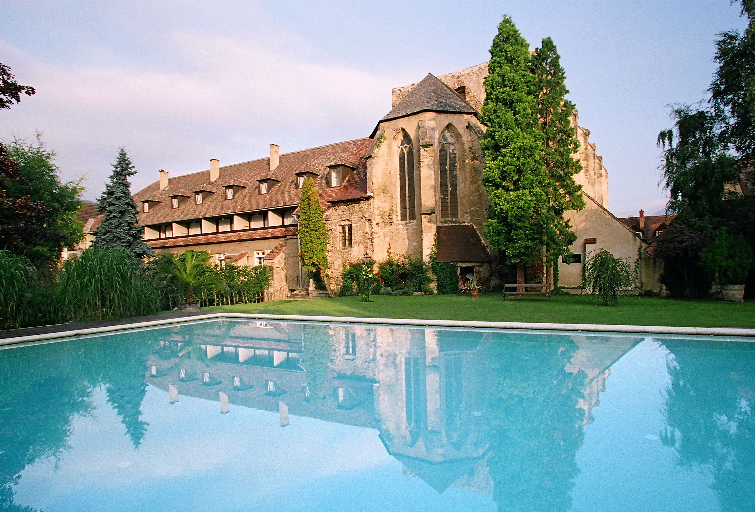 Historisches Gebäude mit Pool im Vordergrund, umgeben von Bäumen und Garten.