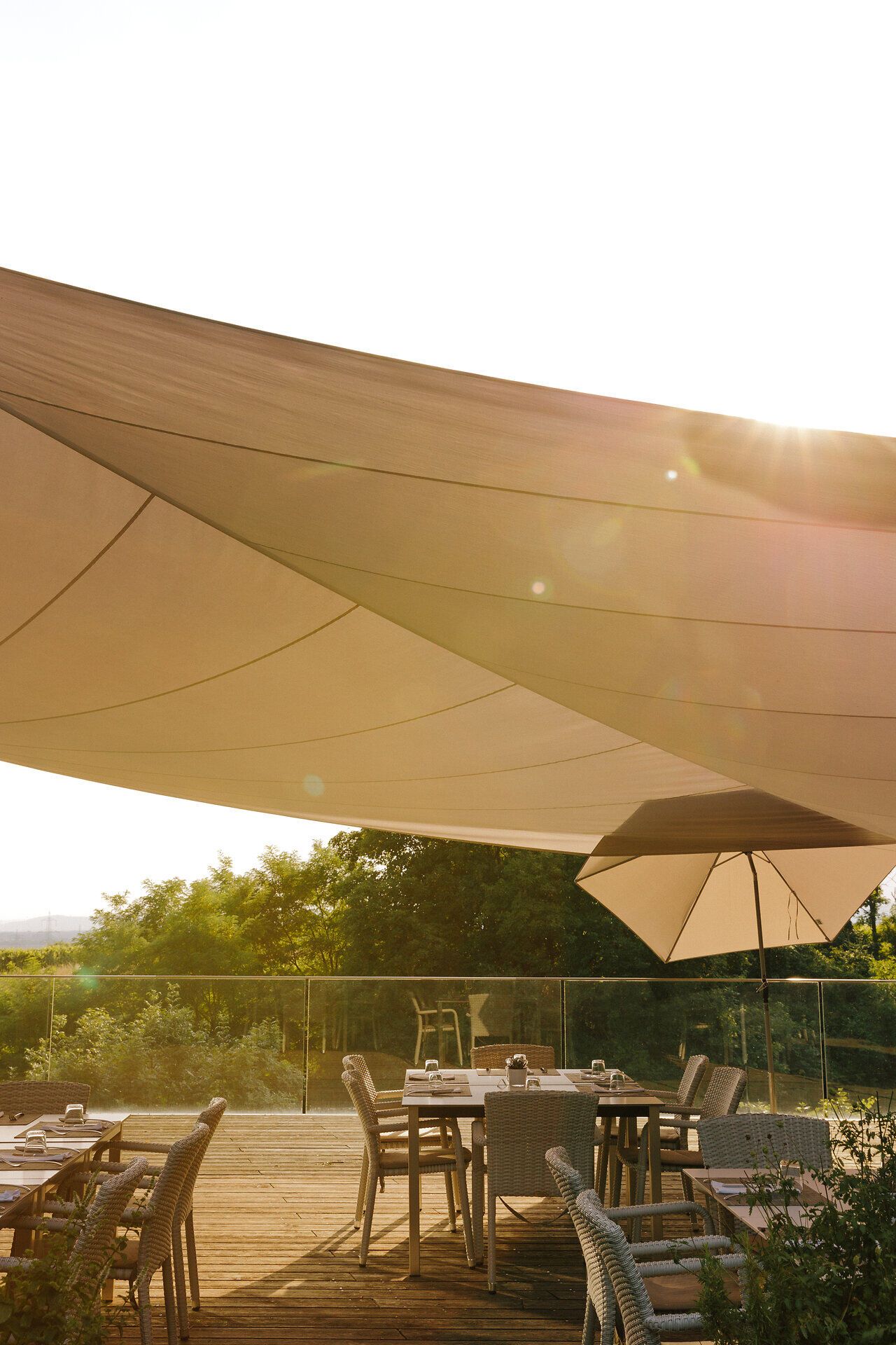 Unter einem sanften Sonnenschein laden die stilvollen Tische und Stühle auf der Terrasse zu einem entspannten Aufenthalt ein. Die sanften Farben des Himmels und die umgebende Natur schaffen eine harmonische Atmosphäre, die zum Verweilen einlädt. Hier kann man die Seele baumeln lassen und die Schönheit der Umgebung genießen.