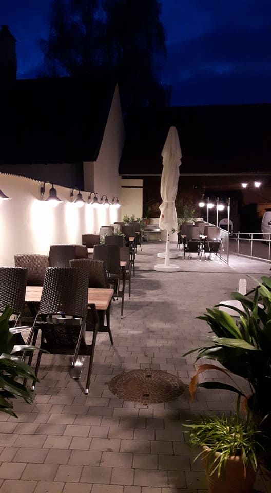 Ein leerer Gastgarten bei Nacht mit Tischen, Stühlen und Pflanzen.