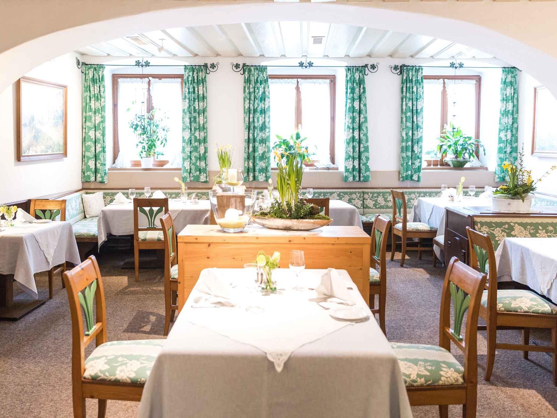 Gemütlicher Gastraum mit Holzmöbeln und grünen Vorhängen.