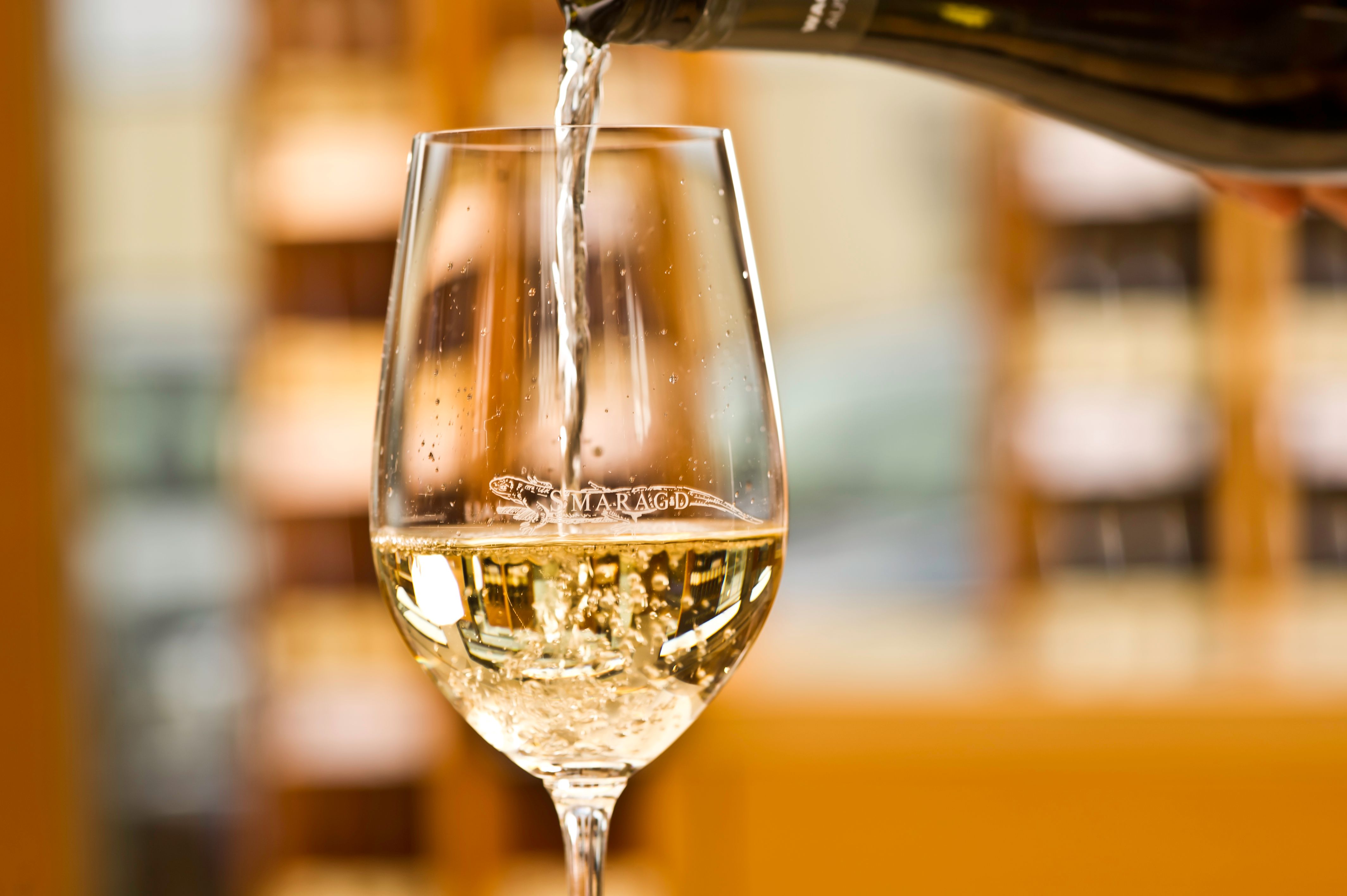 Weißwein wird von der Flasche in ein Weinglas eingeschenkt.