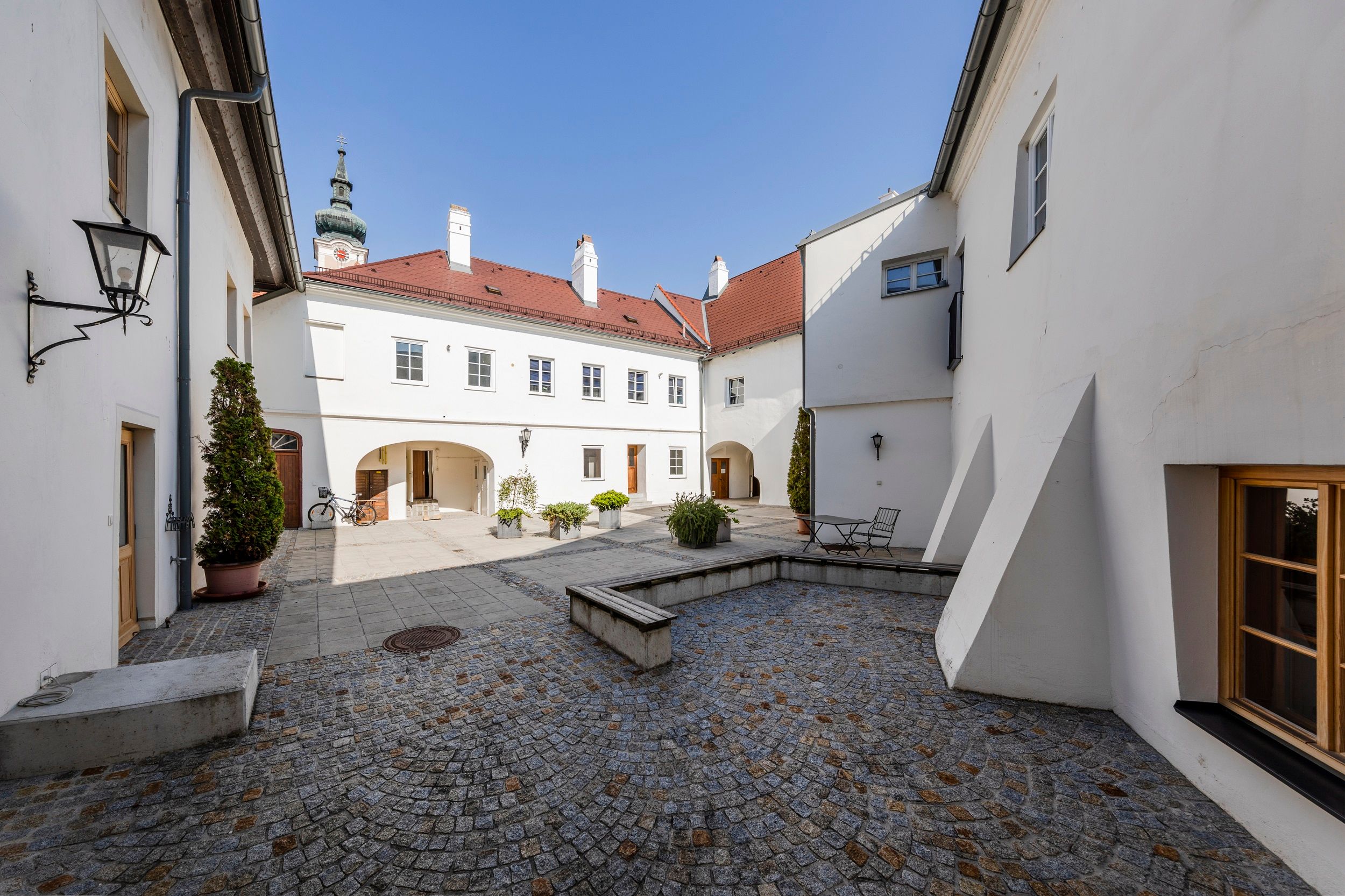Innenhof der TDR-FineArtGallerie in Traismauer mit Kopfsteinpflaster und weißen Gebäuden.