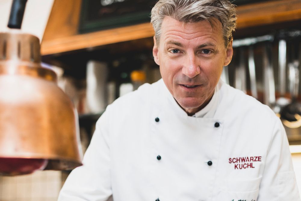 Koch in weißer Uniform in einer Küche mit Kupferlampe.