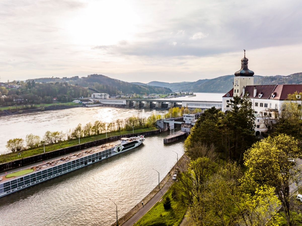 Blick vom linken Donauufer auf das Donaukraftwerk Ybbs-Persenbeug mit Schloss Persenbeug und einem Schiff bei der Einfahrt in die Schleusenkammer.