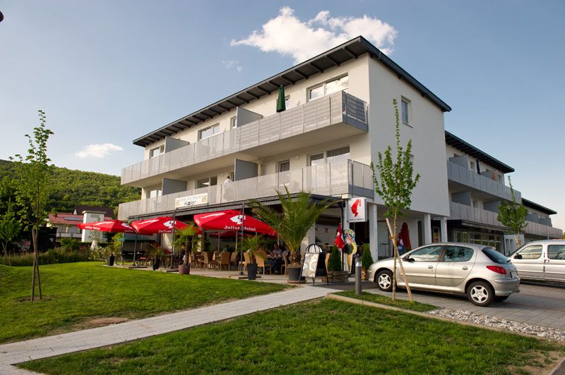 Außenansicht eines modernen Gebäudes mit Café und roten Sonnenschirmen.