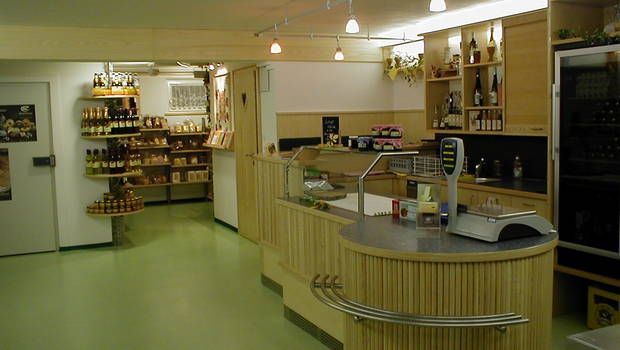 Pohled do interiéru včelařského obchodu s prodejní plochou a regály plnými medových produktů.