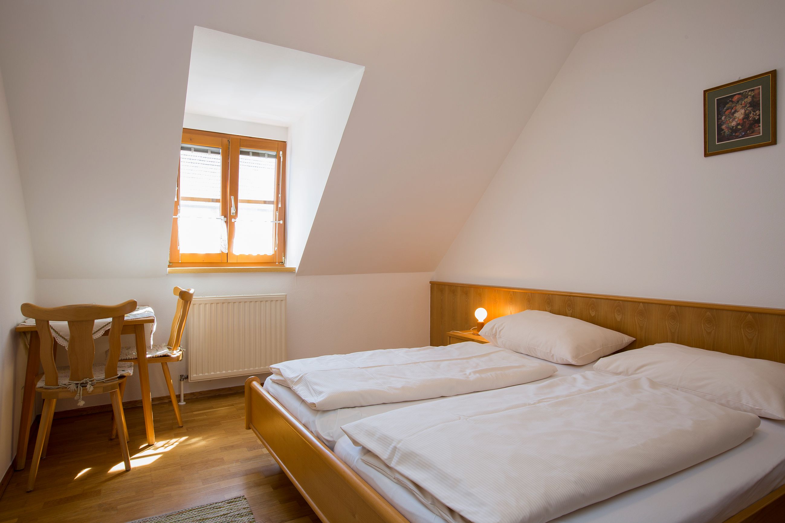 Ein einfach eingerichtetes Schlafzimmer mit einem Doppelbett, einem kleinen Tisch und Stuhl unter einem Dachfenster.