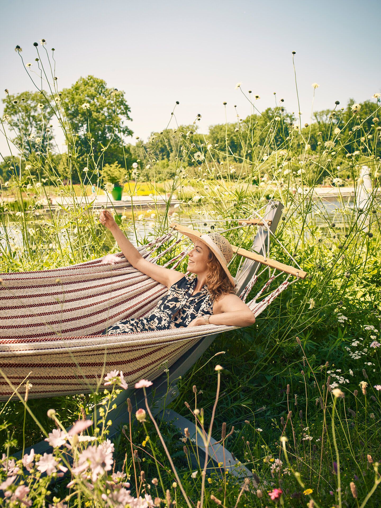 Inmitten üppiger Pflanzen und blühender Wiesen lädt eine gemütliche Hängematte zum Entspannen ein. Die sanften Wellen der Donau im Hintergrund schaffen eine friedliche Atmosphäre, die den Sommer in vollen Zügen genießen lässt.