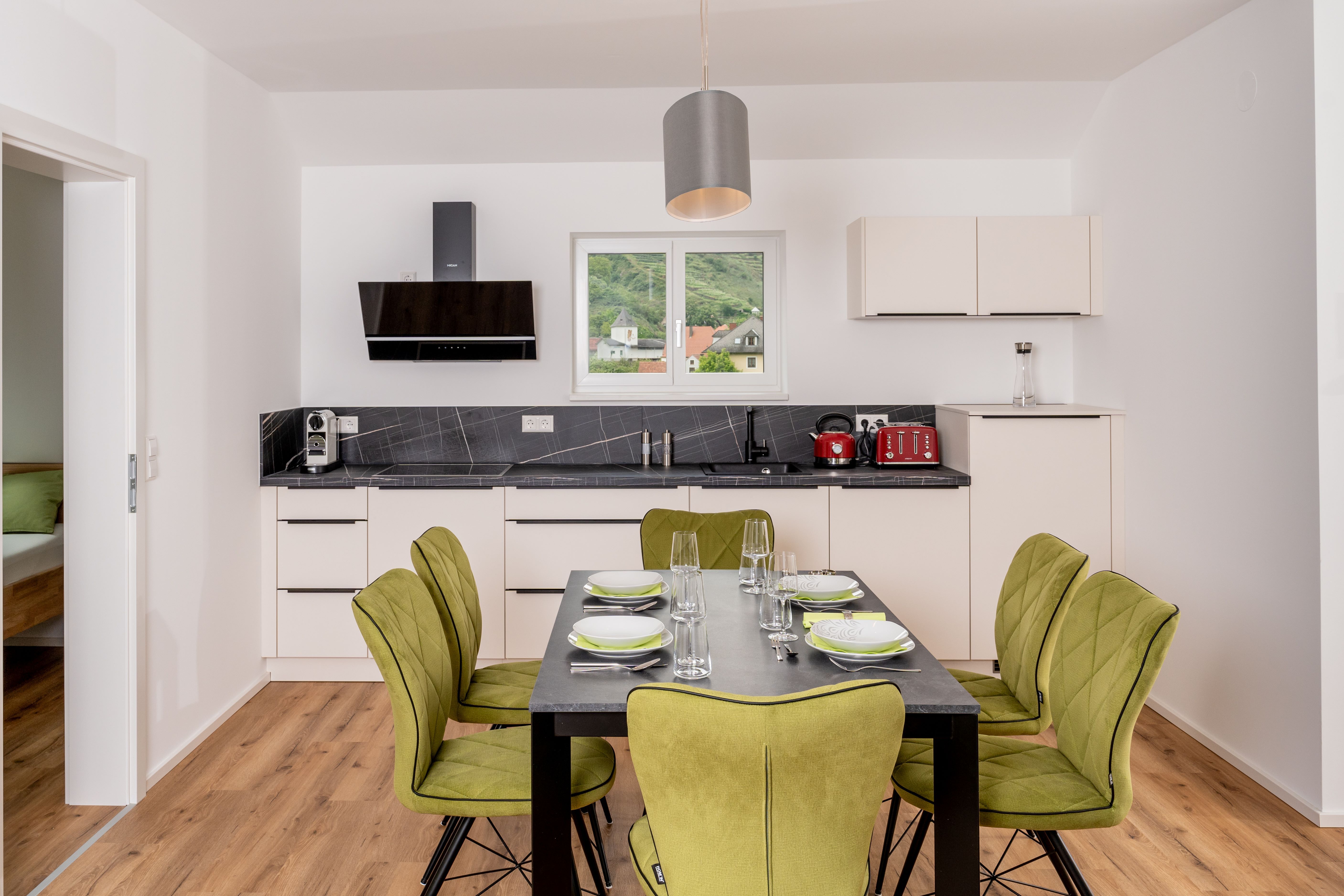 Moderne Küche mit Esstisch und grünen Stühlen, Fenster mit Blick auf Hügel.