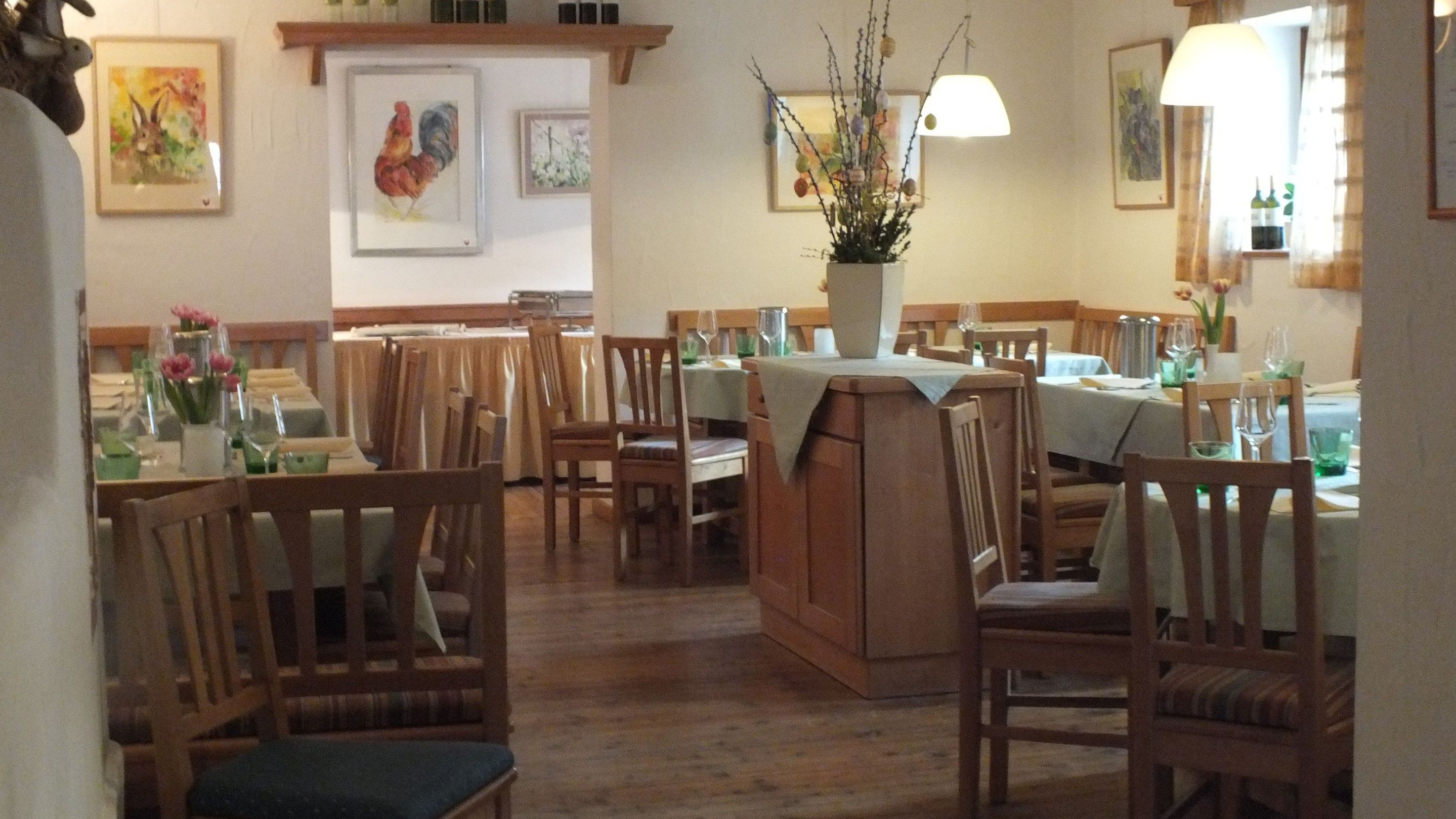 Gemütliches Restaurant mit Holzmöbeln, gedeckten Tischen und Blumenvasen. Bilder von Tieren an den Wänden.