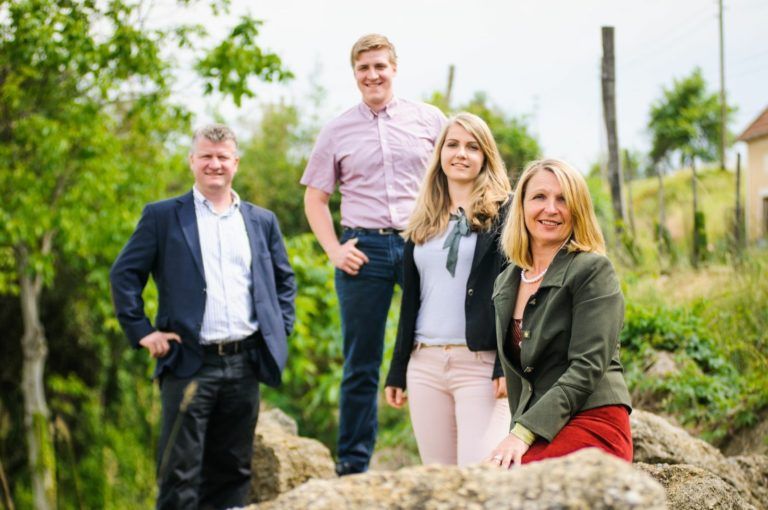 Vier Personen posieren draußen auf einem Felsen, umgeben von Bäumen und Pflanzen.
