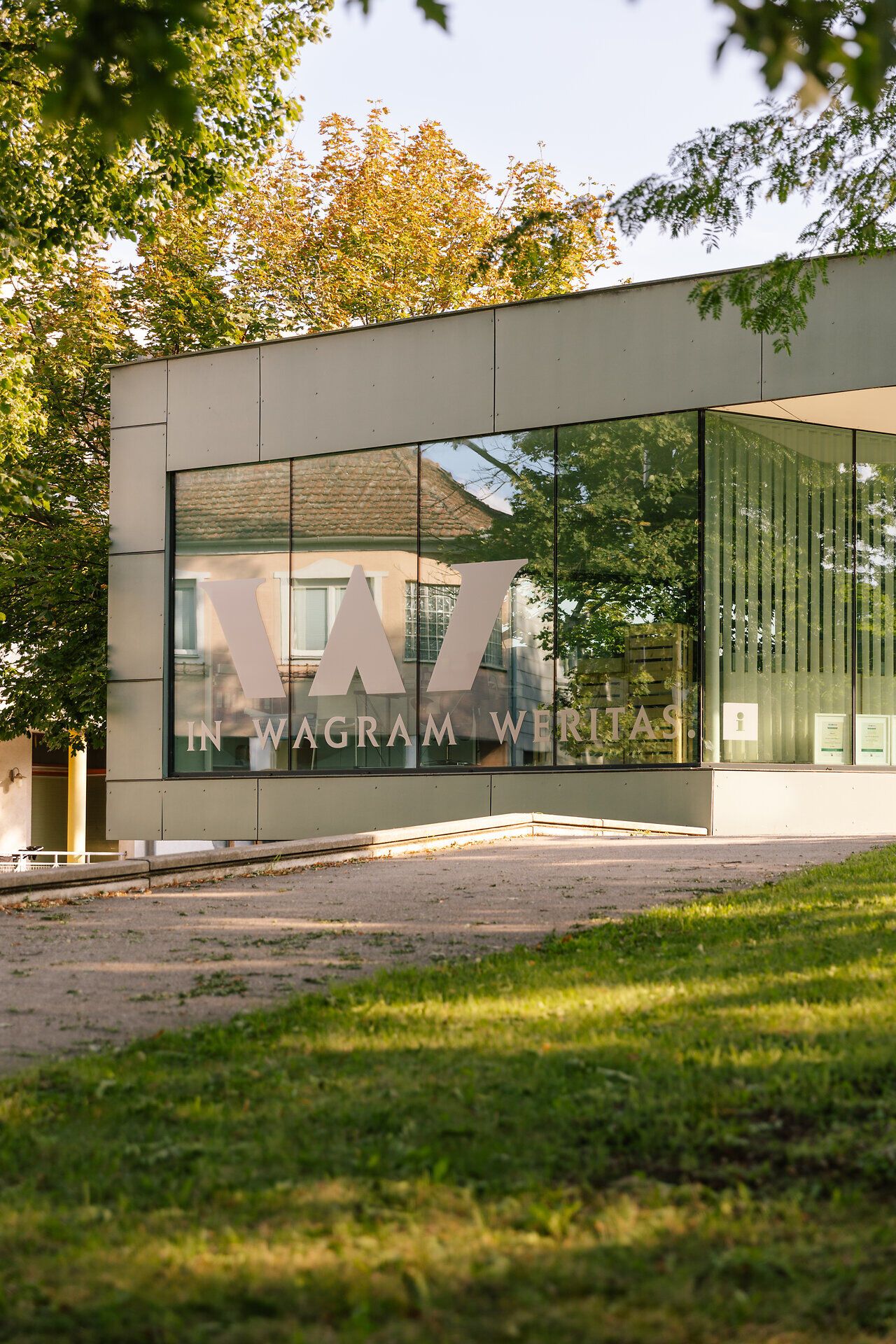 Die moderne Vinothek strahlt eine einladende Atmosphäre aus, umgeben von üppigem Grün und sanften Hügeln. Hier können Besucher die erlesenen Weine der Region genießen und sich von der Schönheit der Landschaft verzaubern lassen.