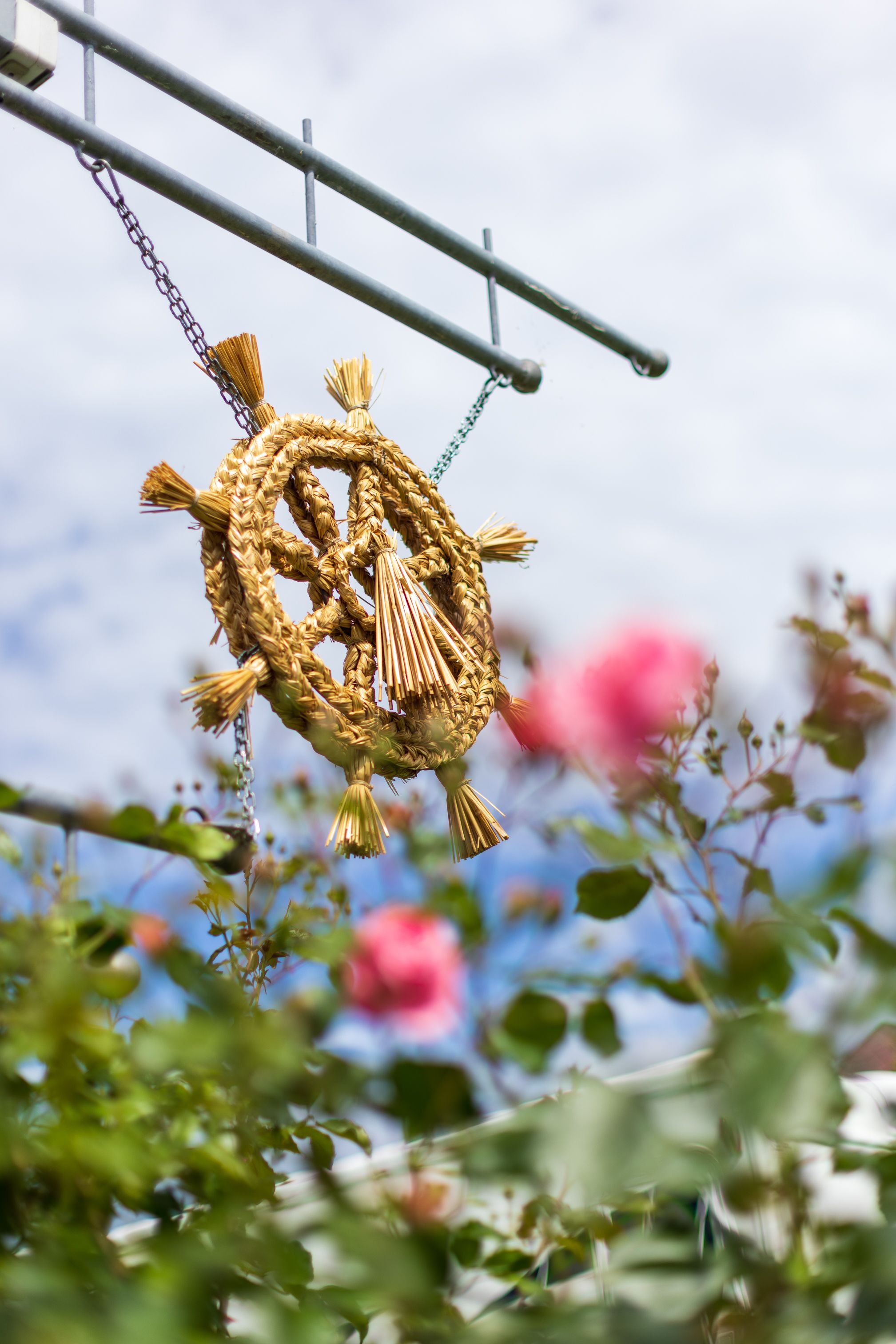 Ein kunstvoll geflochtener Kranz aus Getreide hängt sanft im Wind und verleiht der Umgebung eine festliche Note. Umgeben von blühenden Rosen und dem strahlend blauen Himmel, lädt dieser Ort dazu ein, die Schönheit der Natur und die Köstlichkeiten der Region zu genießen.