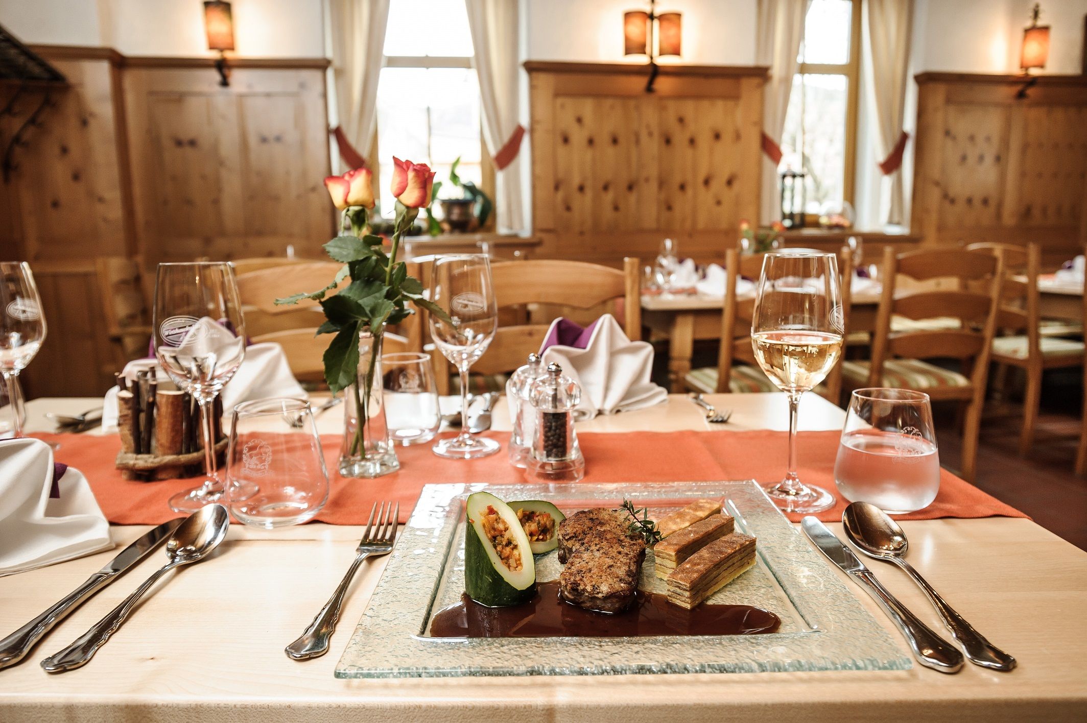 Ein elegant gedeckter Tisch in einem rustikalen Restaurant mit einem Teller Gourmet-Essen, Weingläsern und einer Vase mit Rosen.