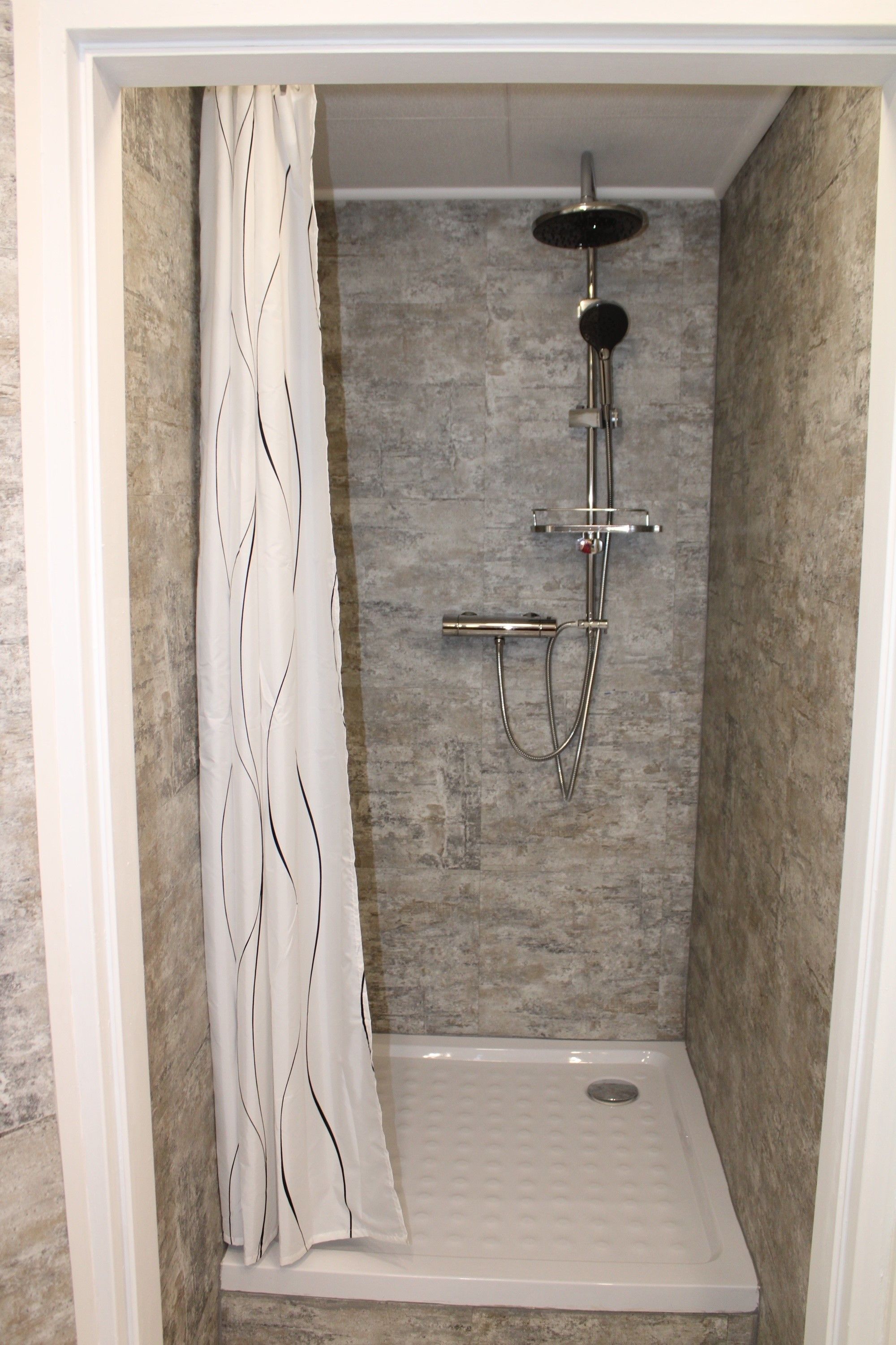 Moderne Dusche mit grauen Fliesen und Duschvorhang.