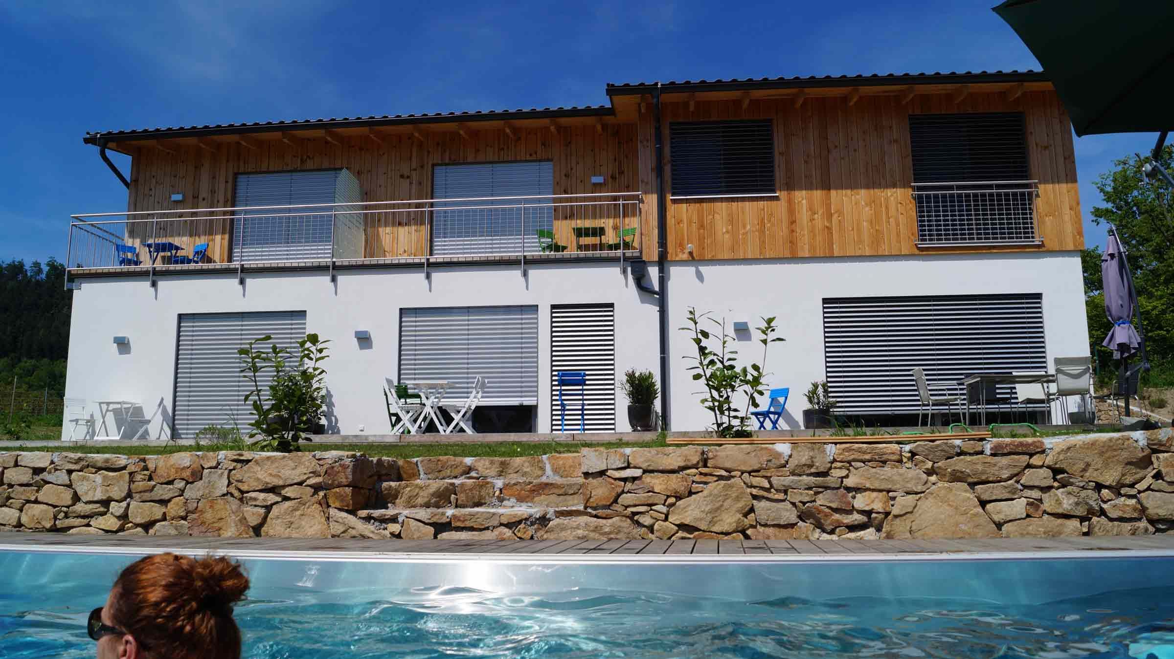 Modernes zweistöckiges Haus mit Holzverkleidung und Pool im Vordergrund.