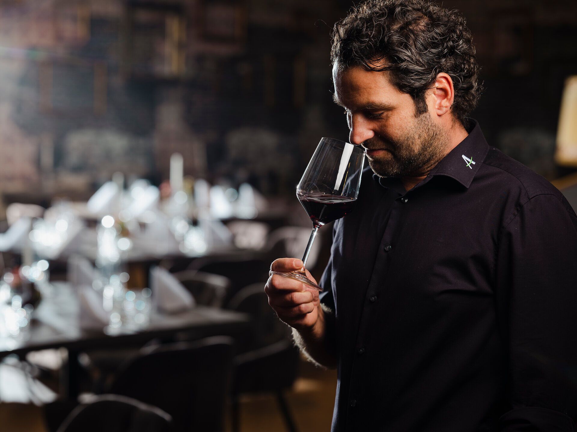 In einem stilvollen Wirtshaus wird ein edler Rotwein genossen, während die warmen Lichtstrahlen eine einladende Atmosphäre schaffen. Der Wirt, mit einem Blick voller Leidenschaft für die Weinkultur, verkostet den Wein und lässt die Gäste an seiner Begeisterung teilhaben.