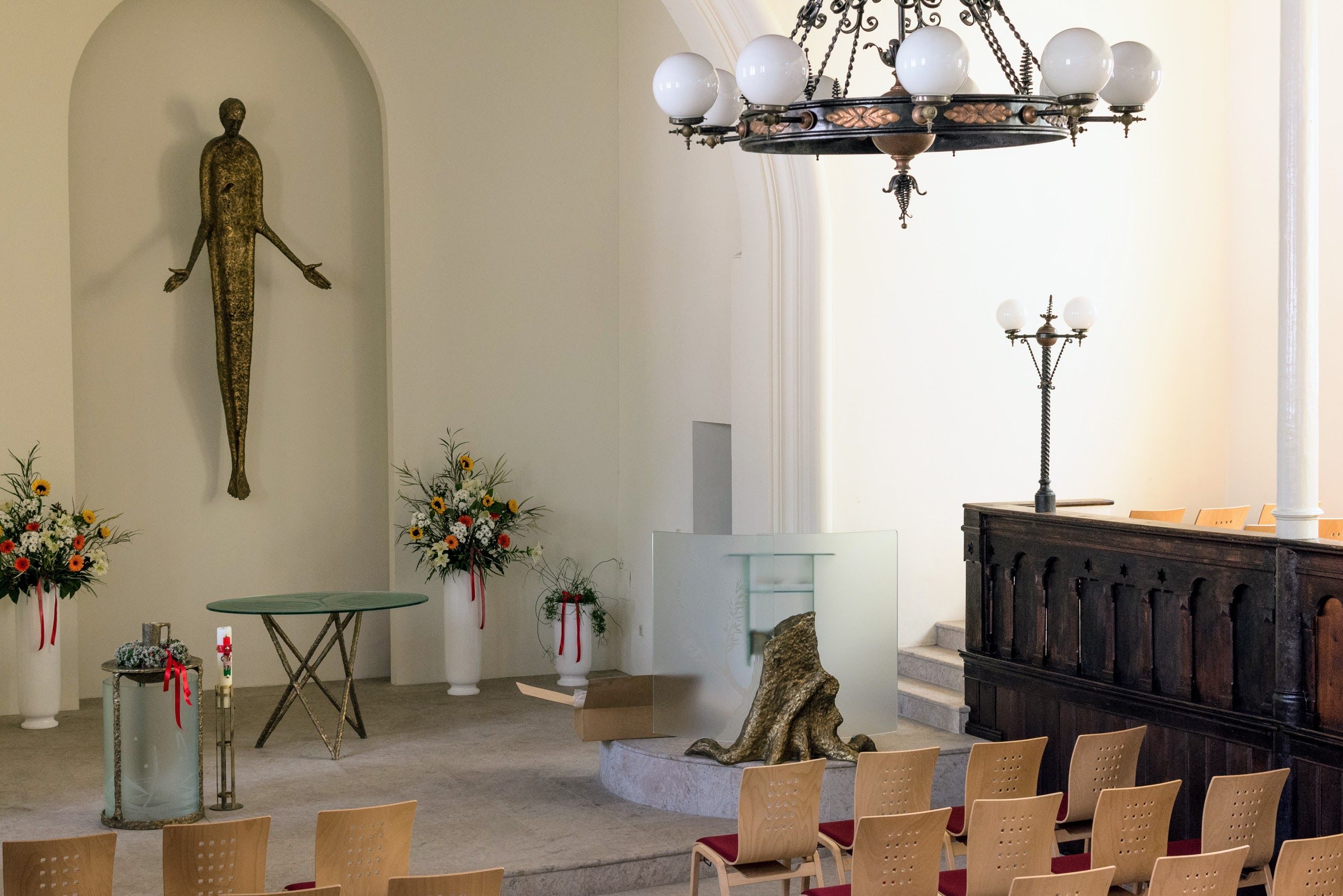 Innenraum einer Kirche mit moderner Dekoration, Blumenarrangements und einer Statue.