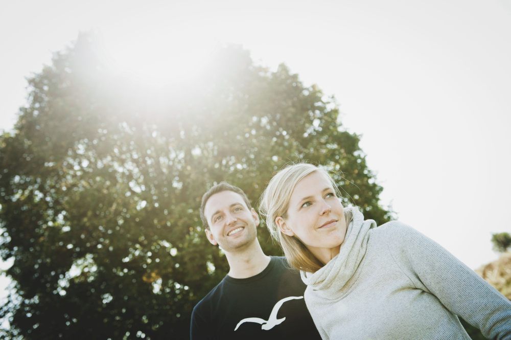 Ein Mann und eine Frau stehen im Freien vor einem Baum, die Sonne scheint durch die Blätter.