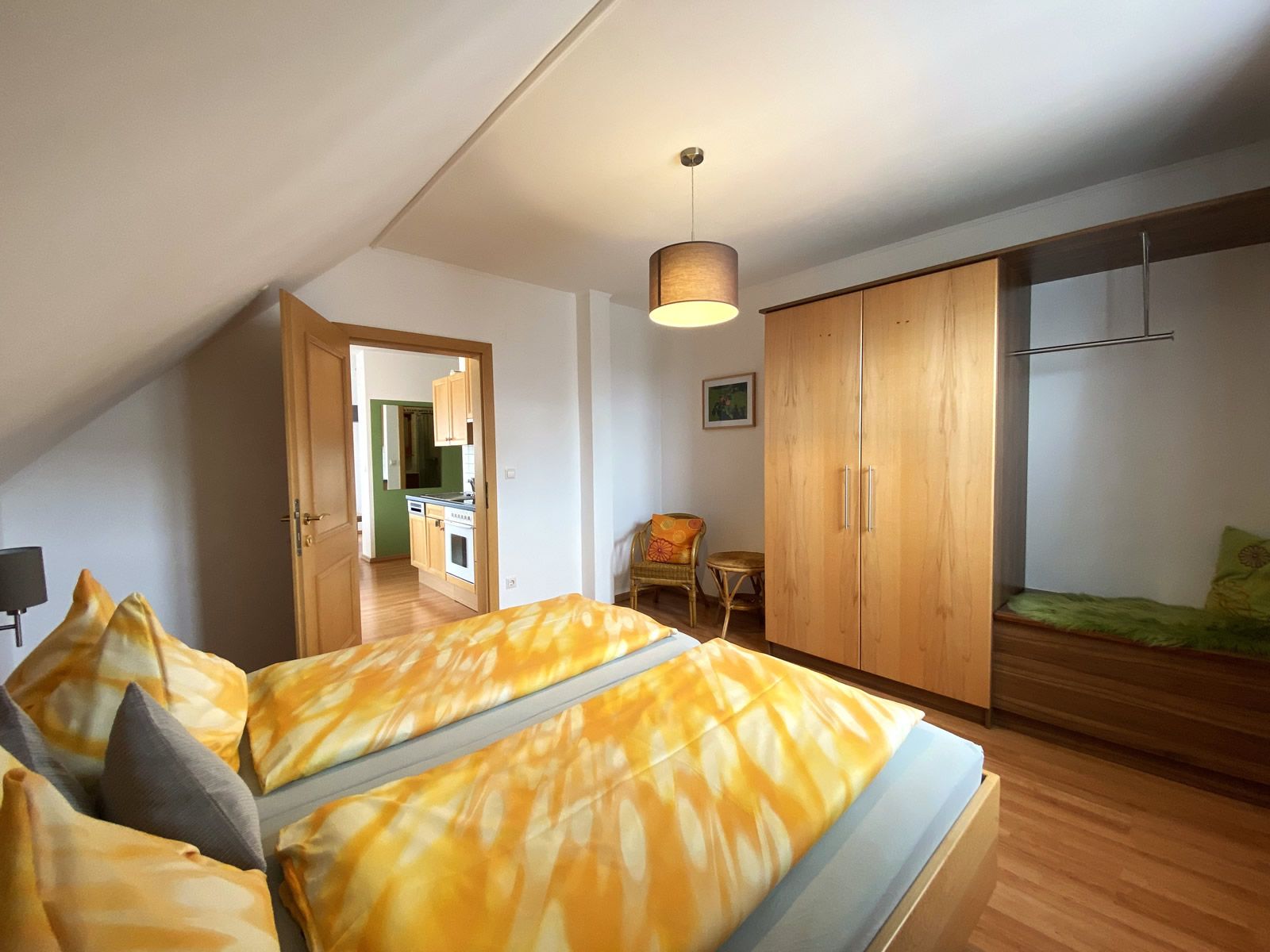 Schlafzimmer mit Doppelbett, Kleiderschrank und Blick in die Küche.