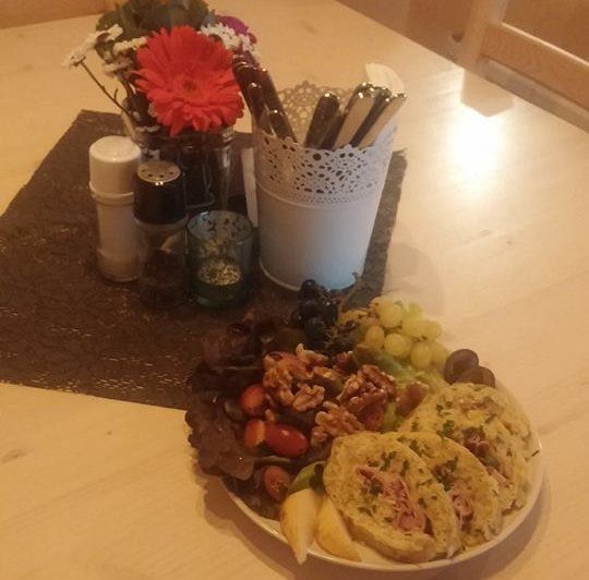 Ein Teller mit Aufschnitt, Nüssen, Trauben und Brot auf einem Tisch mit Blumen und Gewürzen.