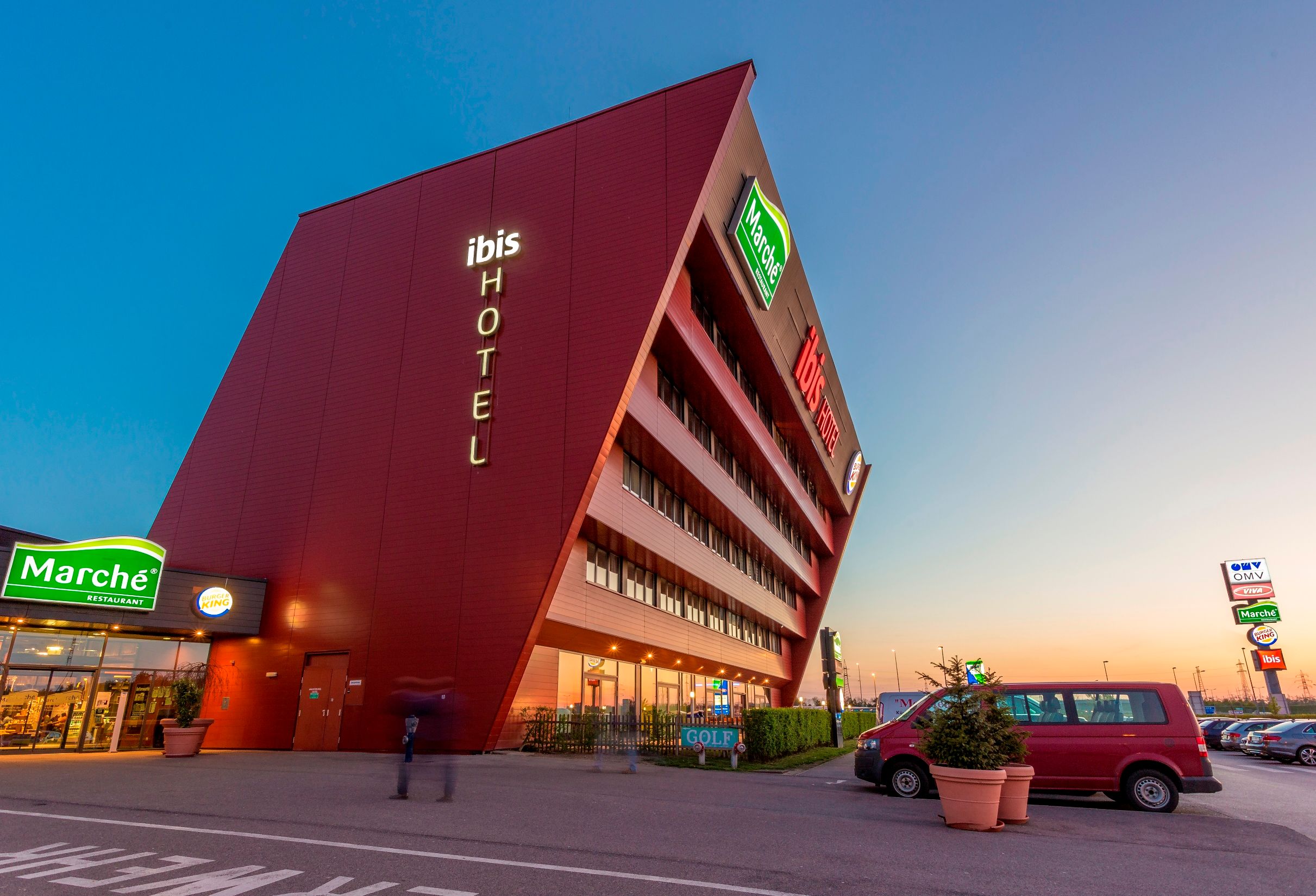 Modernes Hotelgebäude mit schräger Fassade und Leuchtschrift 'ibis HOTEL'.