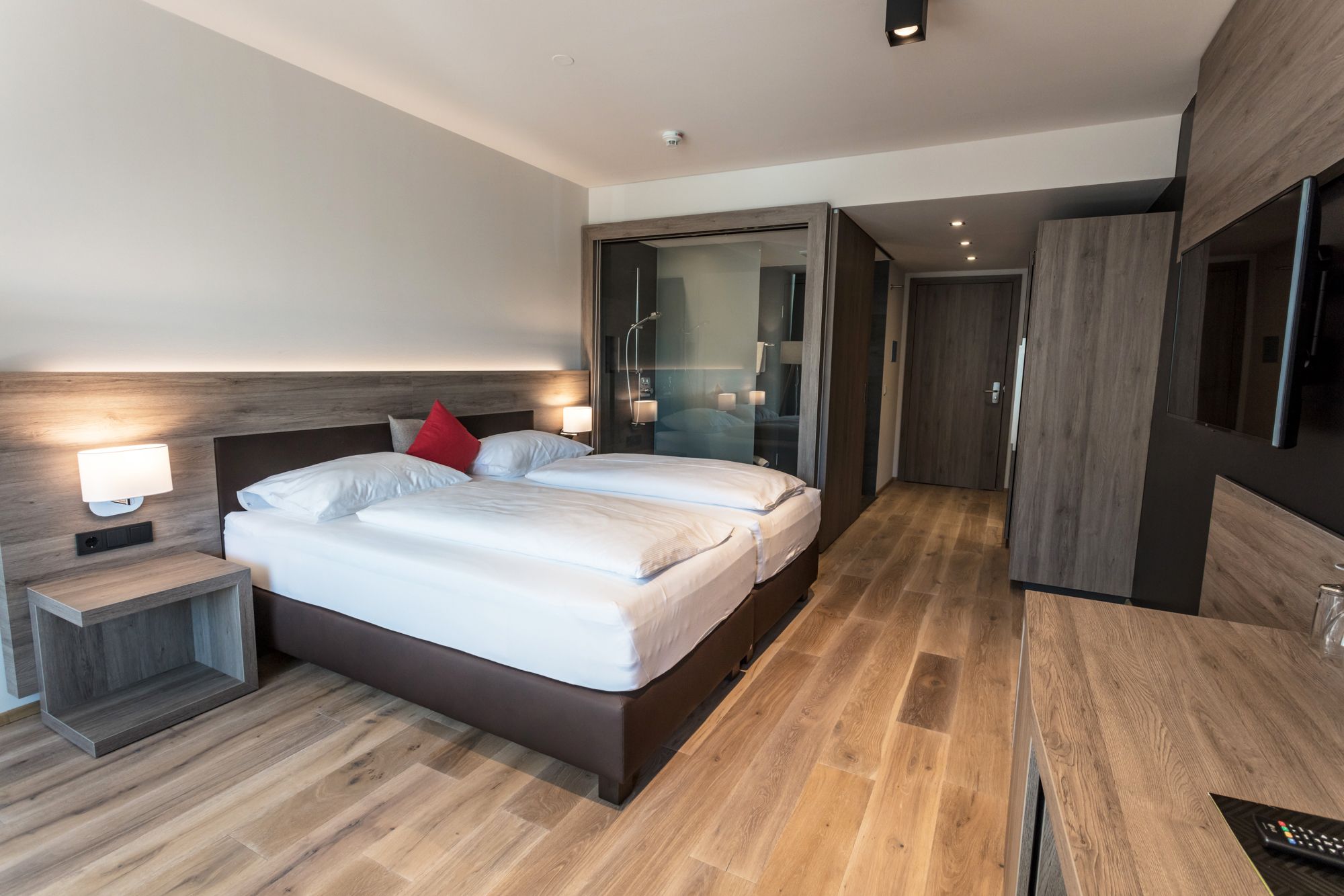Modernes Hotelzimmer mit Doppelbett, Holzboden und Glasdusche.