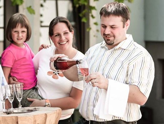 Ein Mann schenkt Sekt in ein Glas ein, während eine Frau und ein Kind zuschauen.