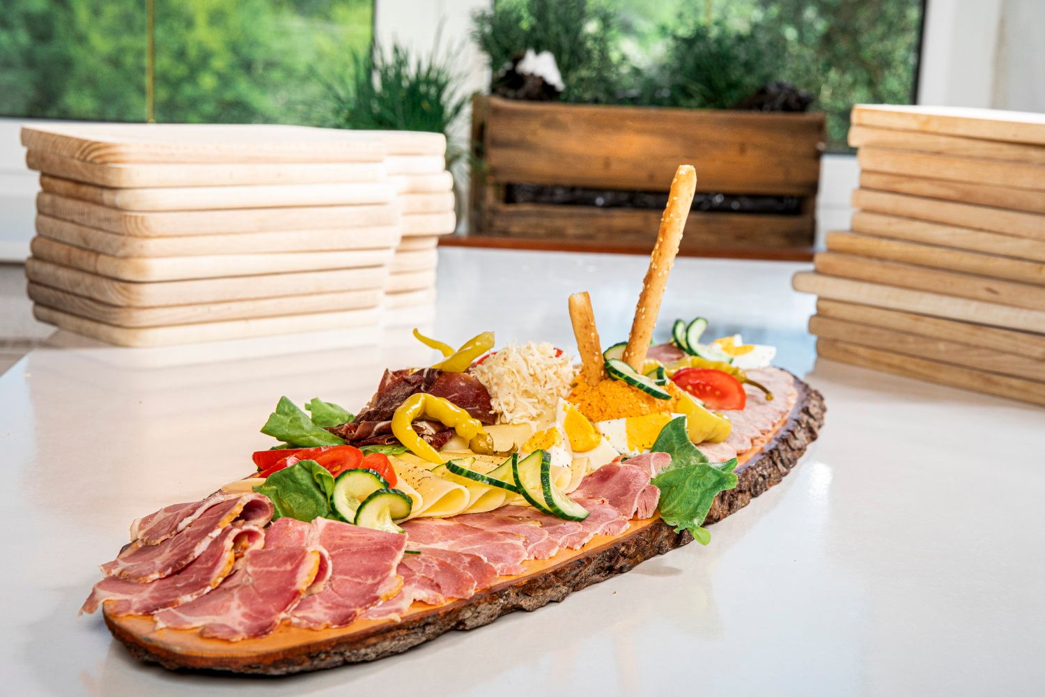 Eine Heurigenplatte mit Schinken, Käse, Gemüse und Brotstangen auf einem rustikalen Holzbrett.