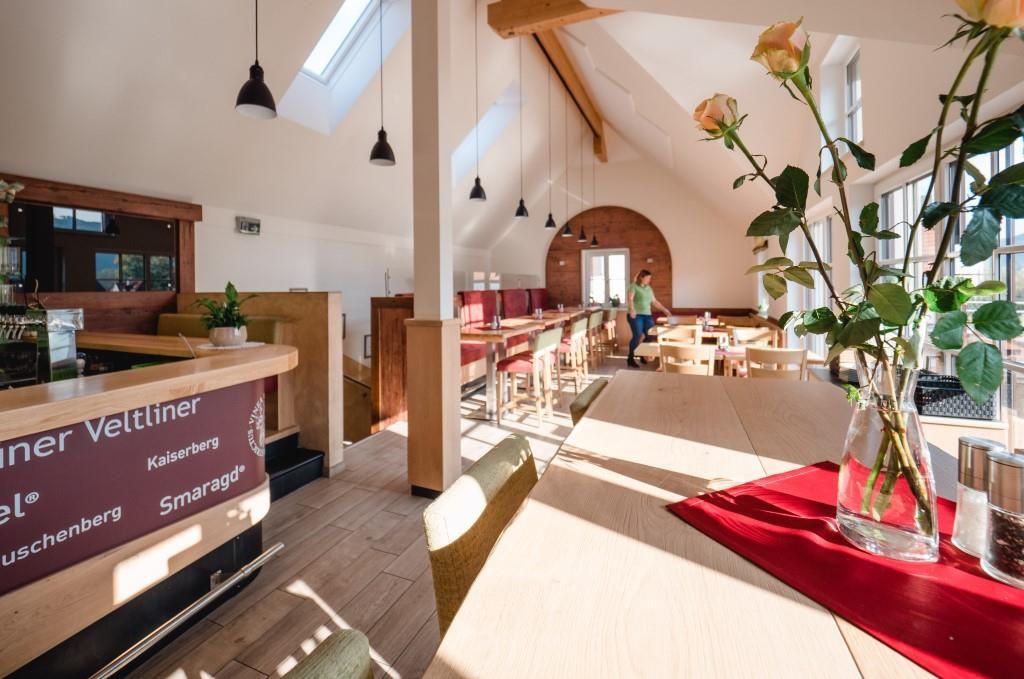 Innenansicht eines modernen Heurigen mit Holzmöbeln und großen Fenstern.