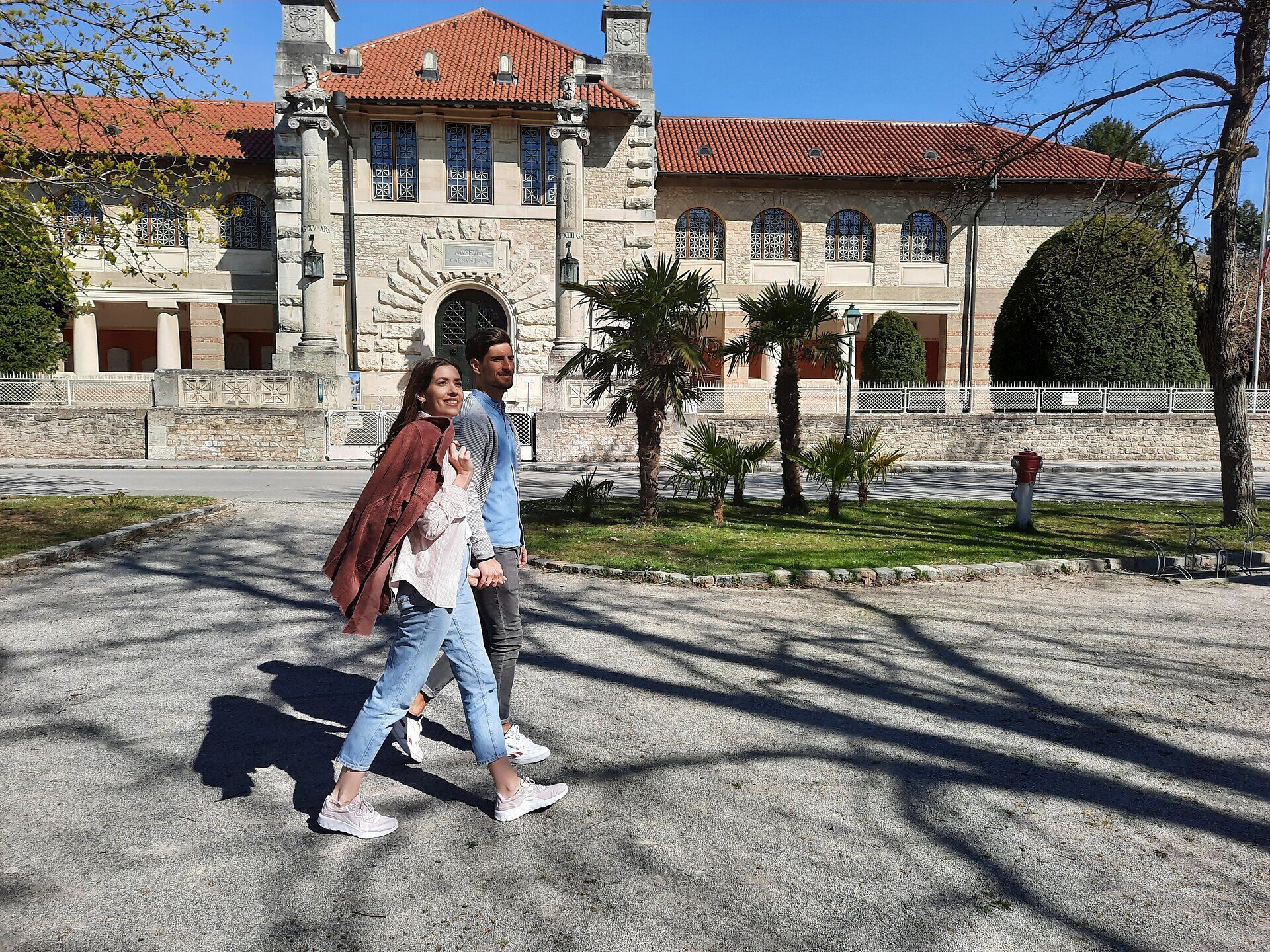 Paar spaziert auf einem Weg, im Hintergrund das Museum Carnuntinum. 