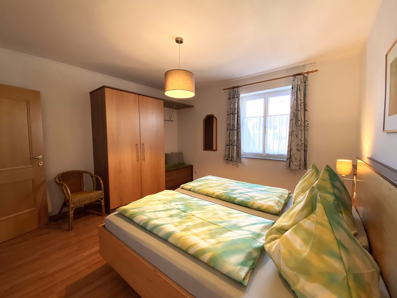 Schlafzimmer mit Doppelbett, Kleiderschrank, Stuhl und Fenster.