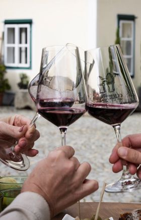 Drei Weingläser mit Rotwein stoßen an, zu sehen sind nur die Hände.