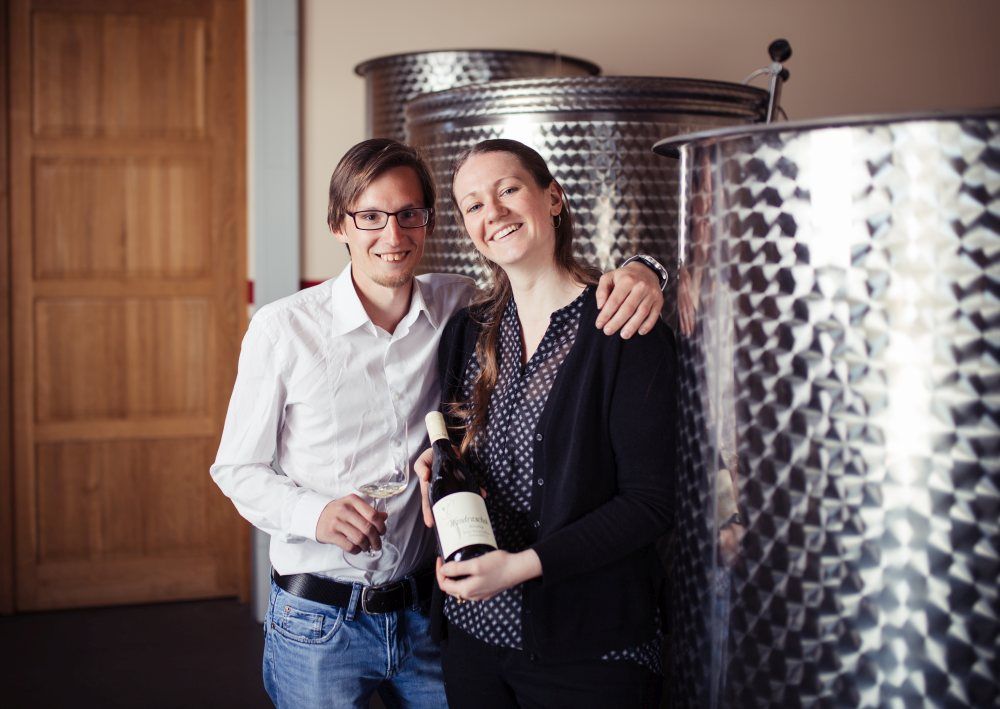 Zwei Personen in einer Weinkellerei mit Weinflasche und Glas.